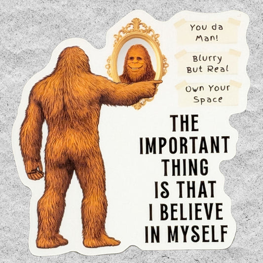 A die-cut sticker featuring a cartoon Bigfoot pointing to a mirror with the text 'You da Man! Blurry But Real! Own Your Space!' and 'THE IMPORTANT THING IS THAT I BELIEVE IN MYSELF' on a light gray textured background.