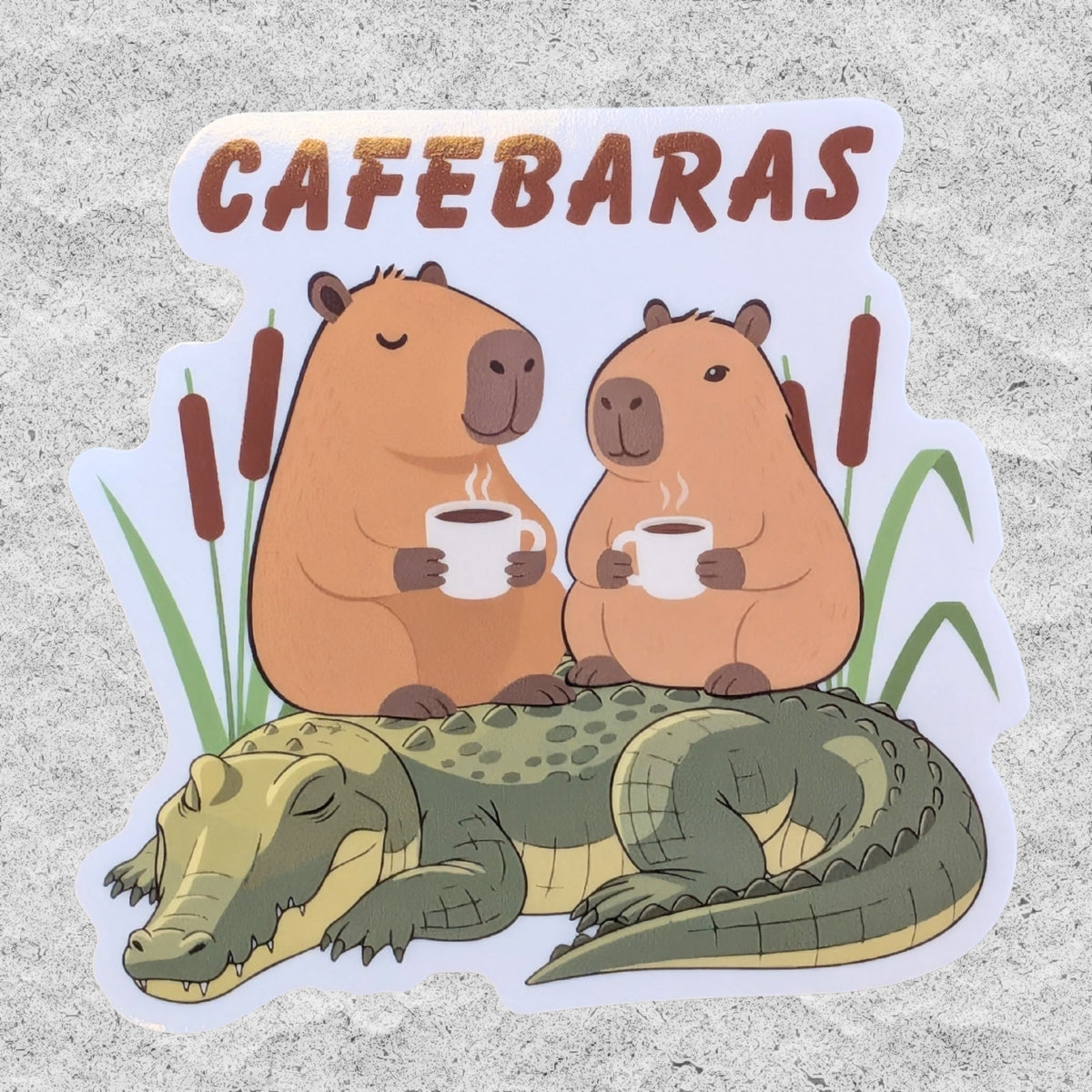 A sticker with two Capybaras sitting on an alligator drinking coffee and the text 'Cafebaras'