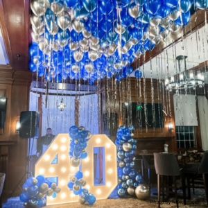Decorative setup with blue and silver balloons and a large '40' sign in a festive room for a party.