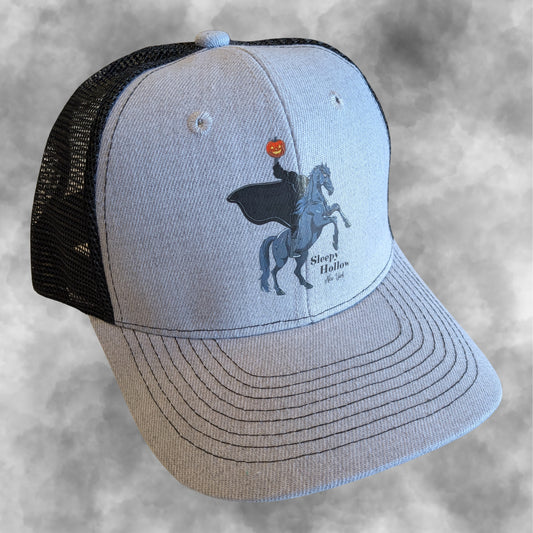 A light gray and black trucker hat featuring a graphic of the Headless Horseman on a rearing horse holding a jack-o-lantern, with the text 'Sleepy Hollow NY' printed on the front panel.
