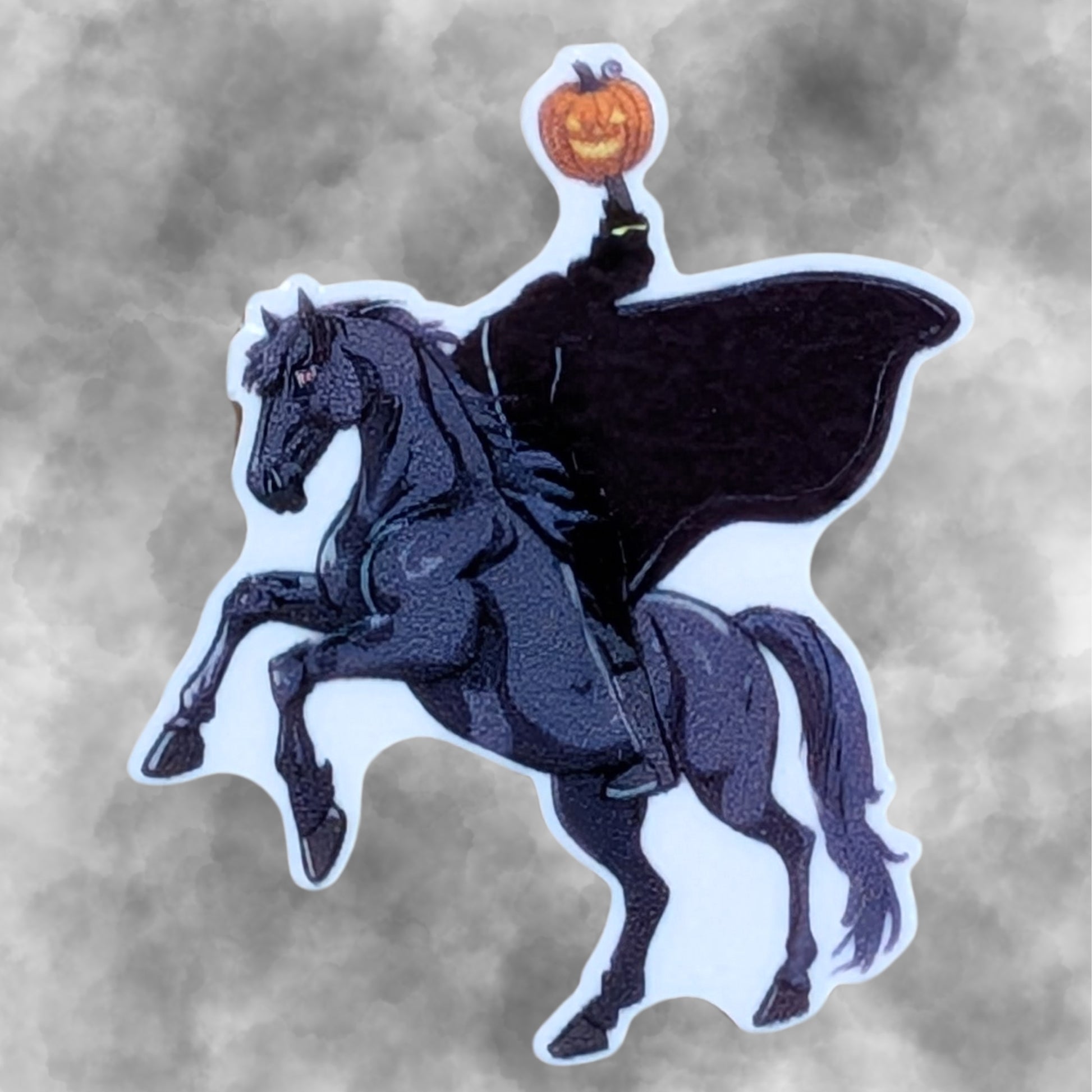 A die-cut temporary tattoo featuring the Headless Horseman on a rearing black horse, holding a glowing jack-o'-lantern, shown against a smoky gray background.