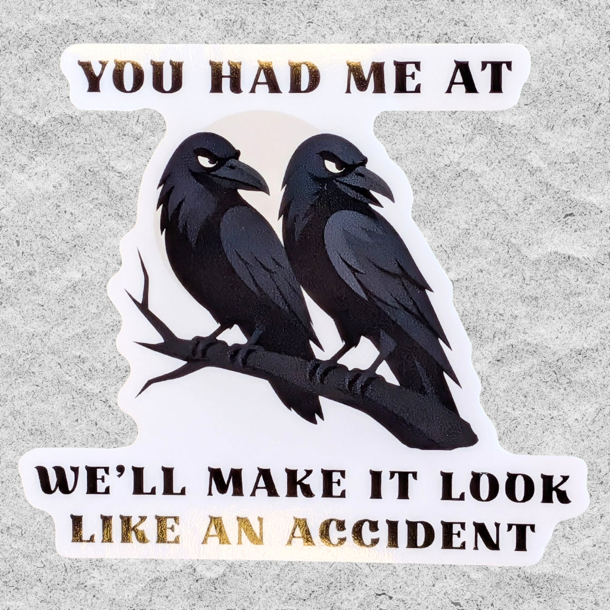 A die-cut vinyl sticker featuring two black crows on a branch with the text 'YOU HAD ME AT WE'LL MAKE IT LOOK LIKE AN ACCIDENT' in black lettering, shown on a textured gray background.