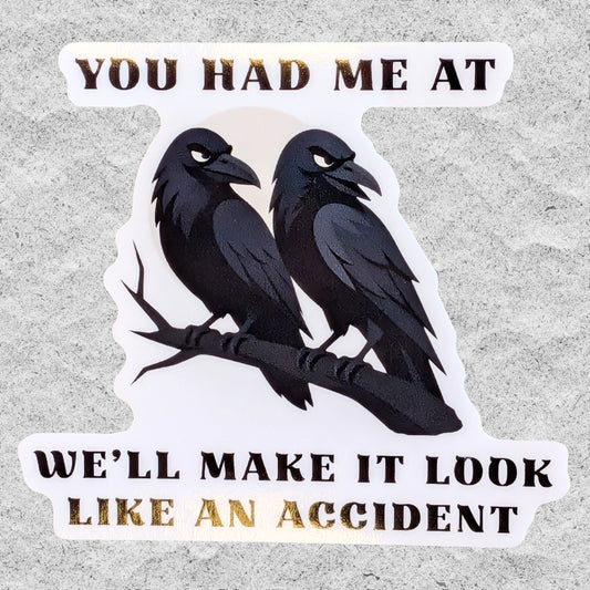 A die-cut vinyl sticker featuring two black crows on a branch with the text 'YOU HAD ME AT WE'LL MAKE IT LOOK LIKE AN ACCIDENT' in black lettering, shown on a textured gray background.