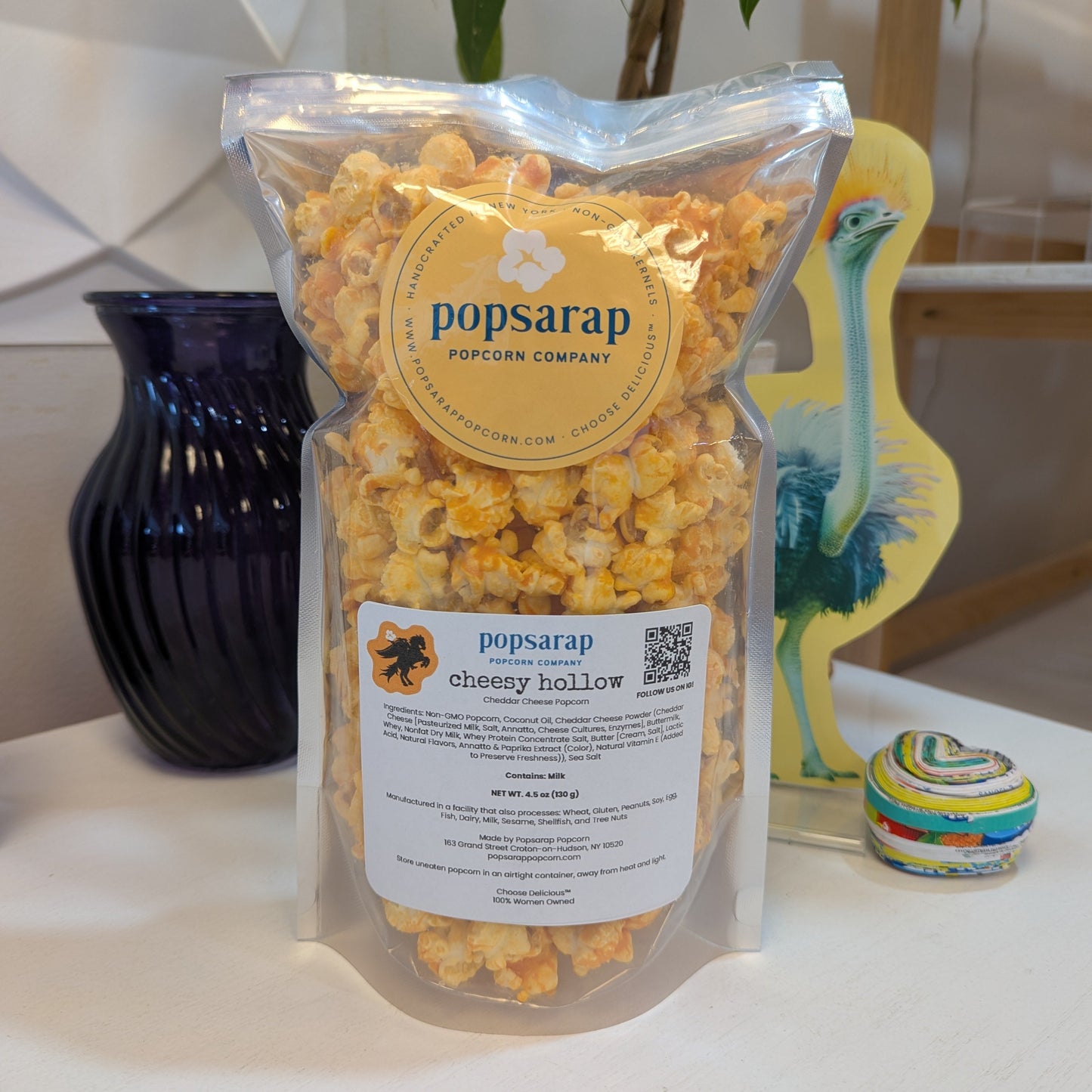 Popsarap Cheesy Hollow popcorn bag on a white table with decorative items in the background