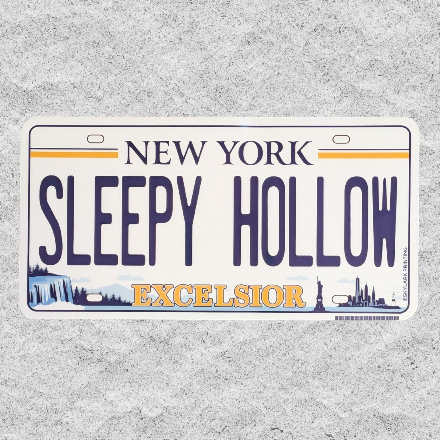 A die-cut sticker of a license plate styled like a New York plate, reading 'SLEEPY HOLLOW' with 'EXCELSIOR' below, photographed on a textured light gray background.