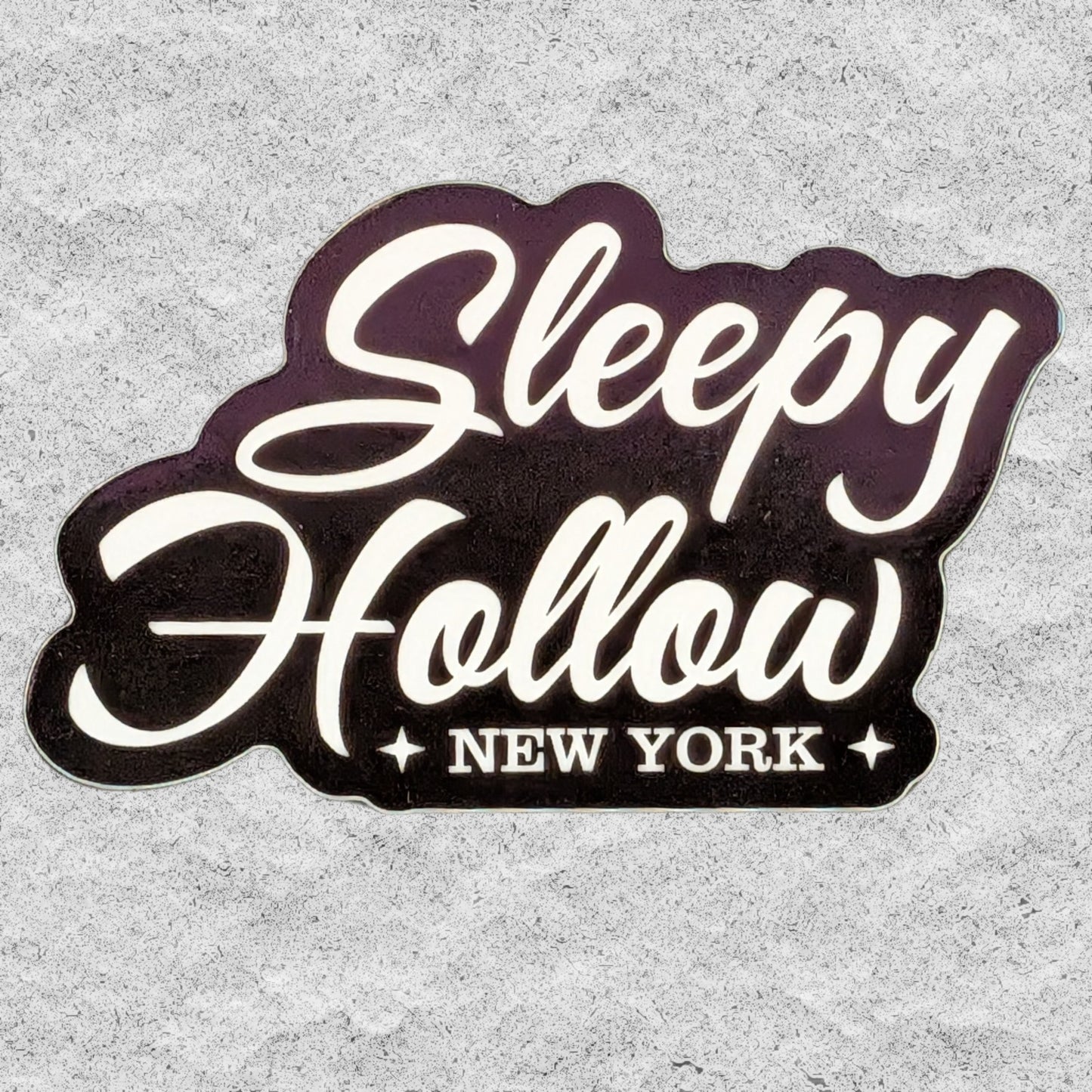 A die-cut sticker with the text "Sleepy Hollow NY" on a textured grey background.
