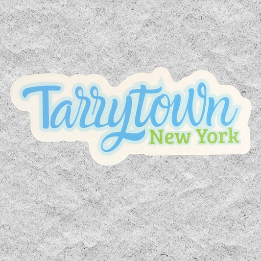 A die-cut sticker featuring the text 'Tarrytown New York' in light blue and green lettering on a white background, shown against a textured gray surface.