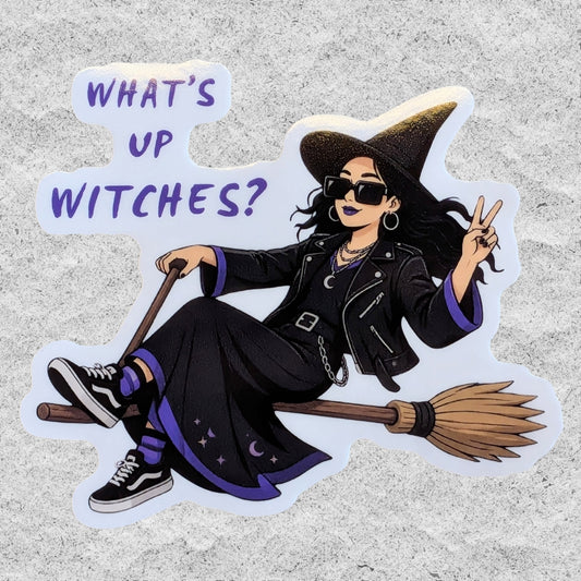A die-cut sticker featuring an illustrated witch sitting on a broomstick with the text 'WHAT'S UP WITCHES?' in purple lettering, shown on a light gray textured background.
