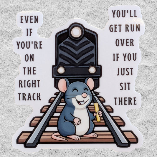 A die-cut vinyl sticker featuring a cartoon gray mouse sitting on train tracks in front of a black train, holding a yellow snack. The left side of the sticker reads 'EVEN IF YOU'RE ON THE RIGHT TRACK' and the right side reads 'YOU'LL GET RUN OVER IF YOU JUST SIT THERE' in dark brown text, all on a white background with a textured gray surface behind it.
