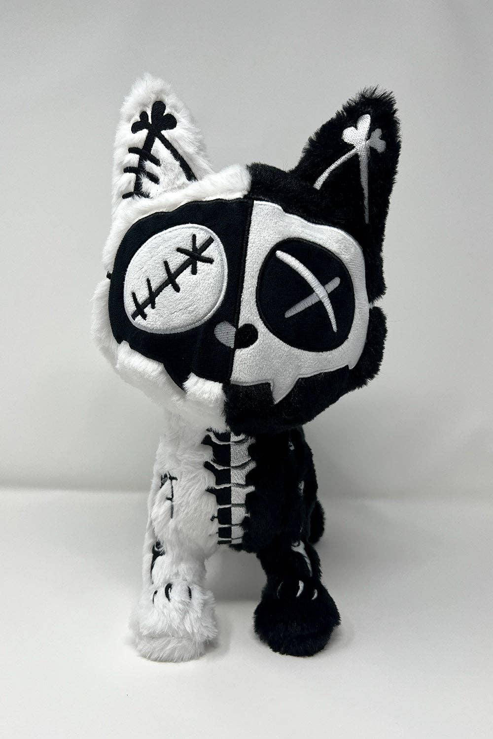 Black and white skeleton cat plush toy on a light gray background