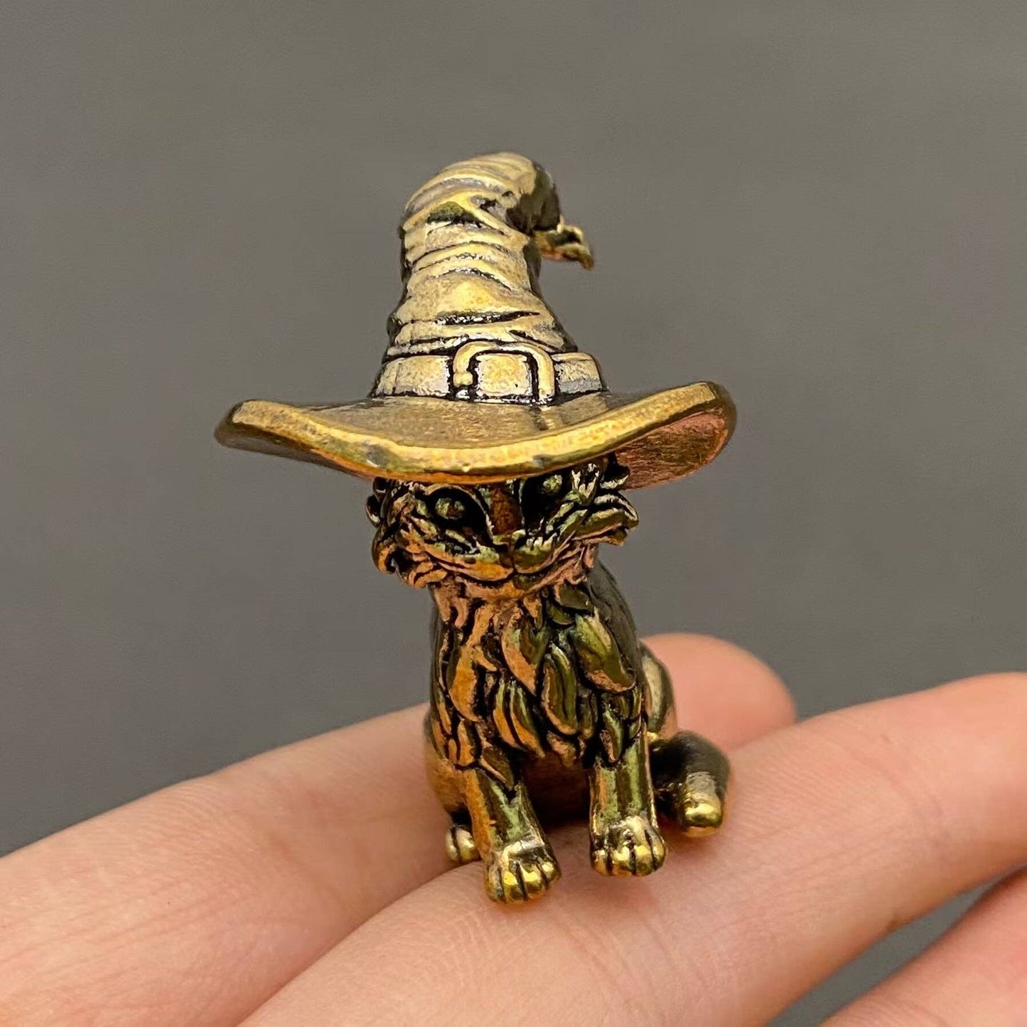 Brass figurine of a kitten with a witch hat held in a hand against a gray background
