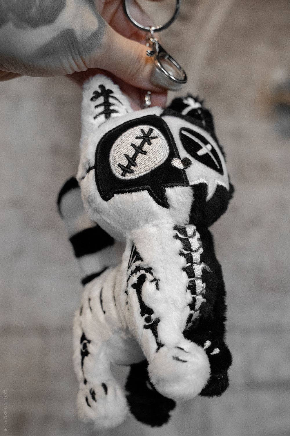 Black and white cat plush toy with skeleton design held by a hand against a blurred background