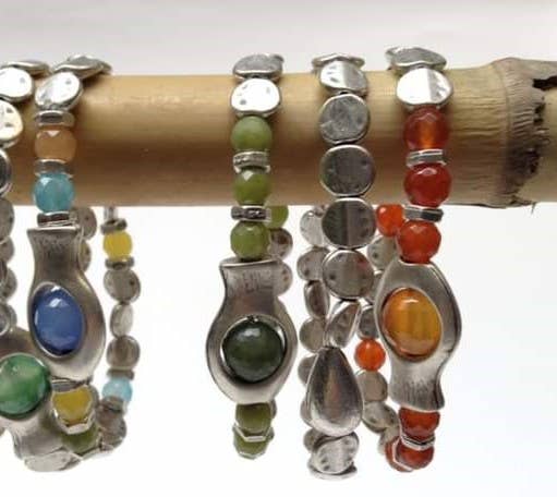 A set of handmade silver beaded bracelets with colorful gemstone accents, displayed on a natural bamboo branch against a white background.