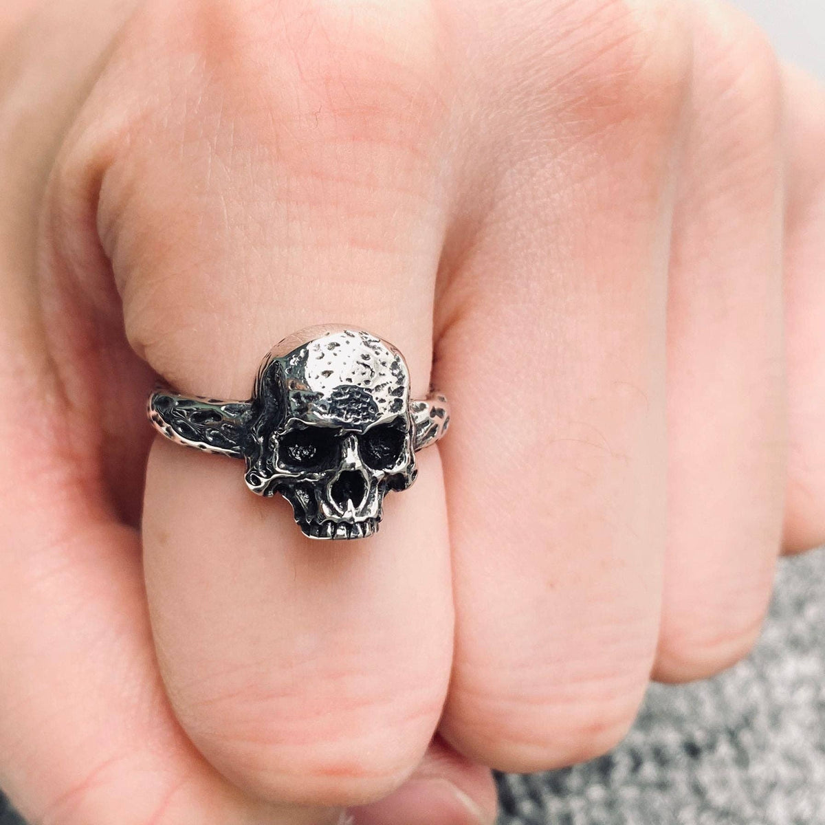 A close-up of a hand wearing a detailed stainless steel skull ring on the middle finger.