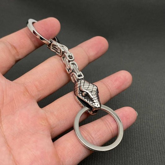 Silver dragon head keychain held in a hand against a dark background