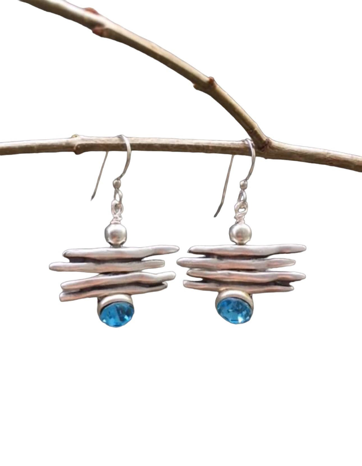 Pair of earrings with blue gemstones and silver accents hanging from a branch.