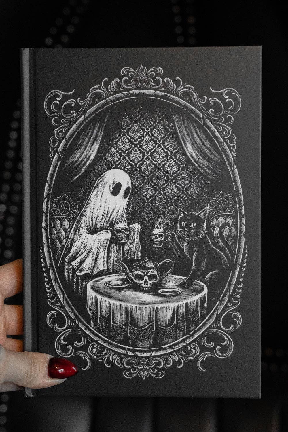 Black journal with a ghost and cat illustration on a dark background