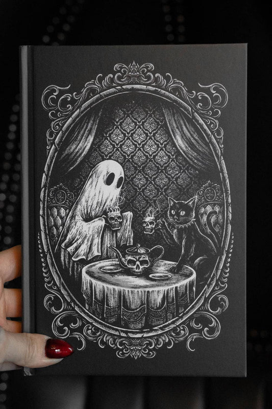 Black journal with a ghost and cat illustration on a dark background