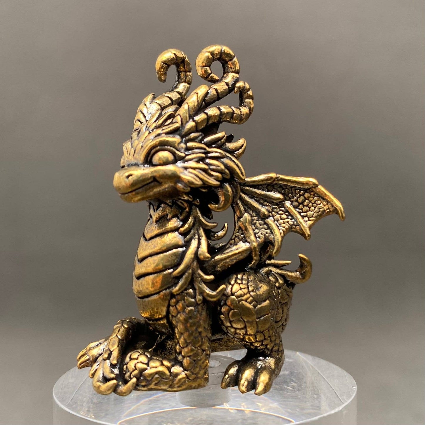 Brass dragon figurine on a clear stand with a gray background