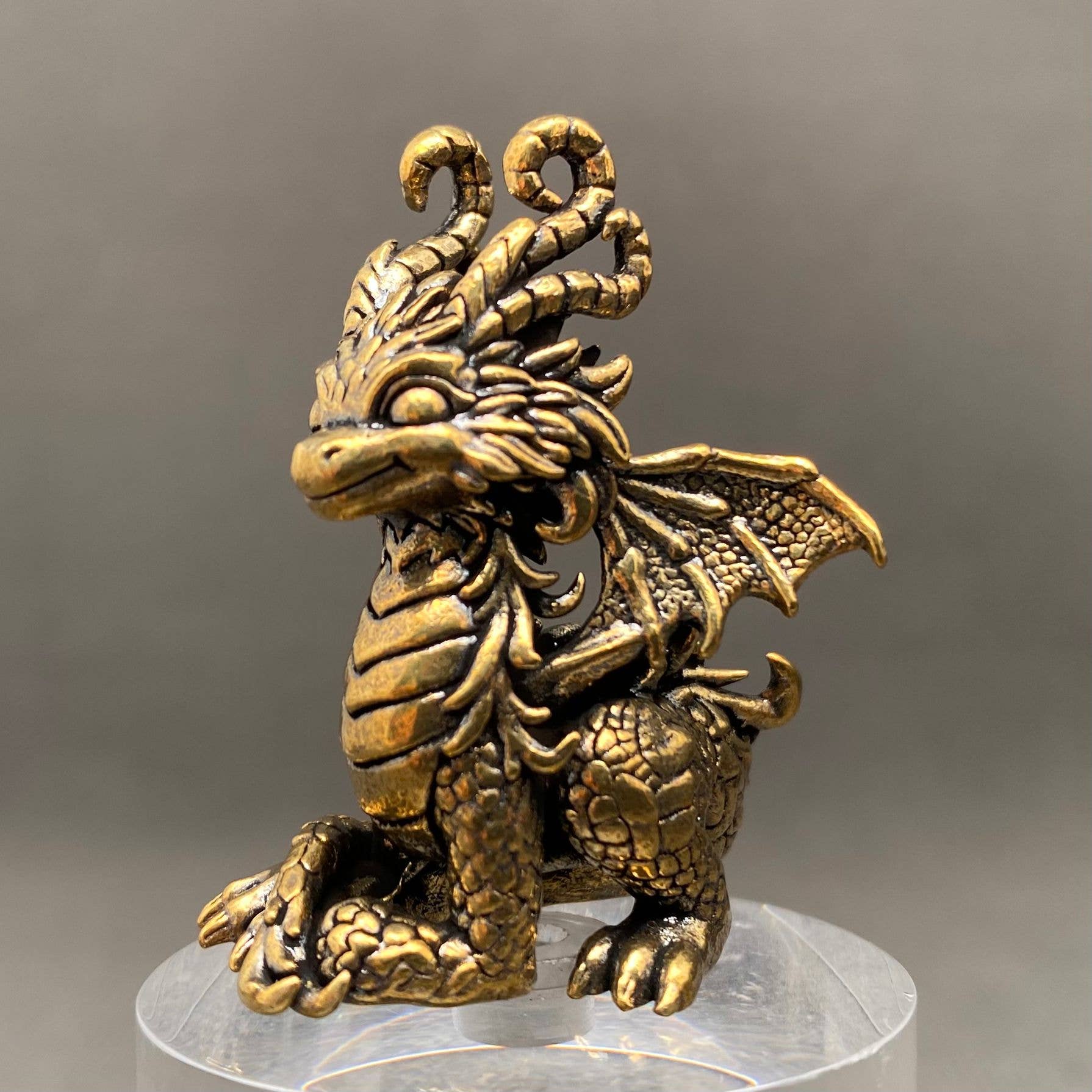 Brass dragon figurine on a clear stand with a gray background