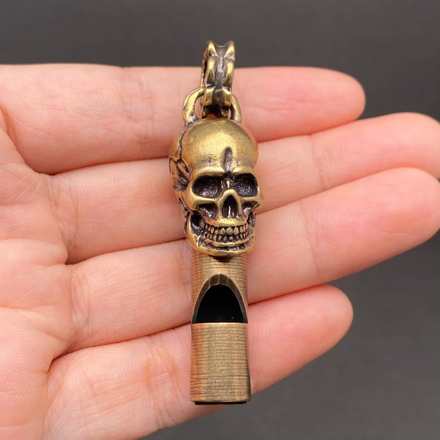 Brass skull-shaped whistle held in a hand against a dark background