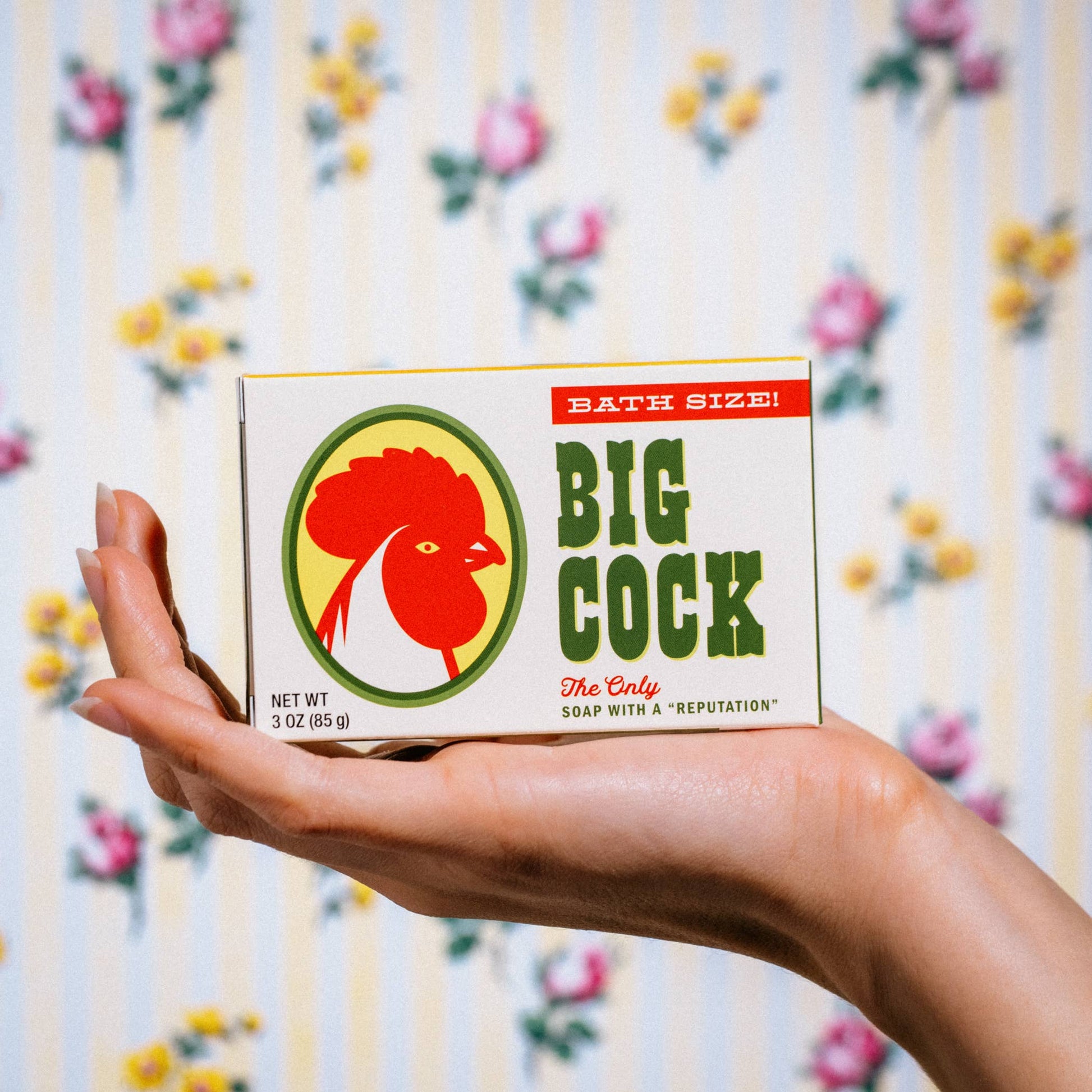 Hand holding a box of Big Cock soap with a colorful background