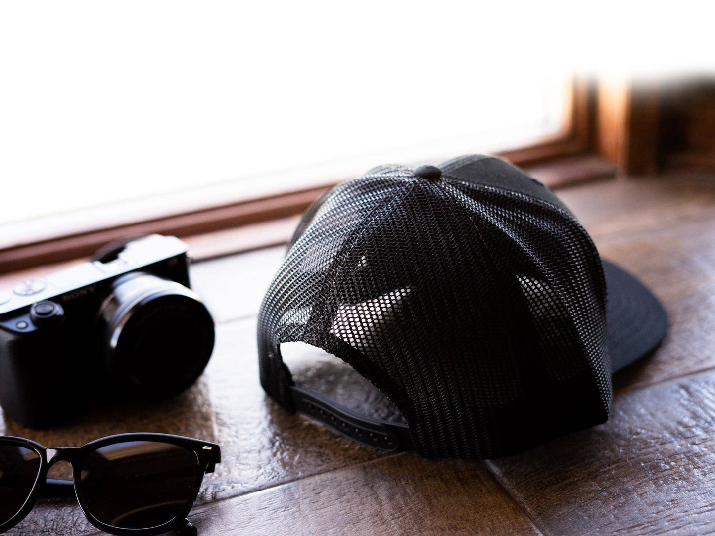 Black mesh cap and sunglasses on a wooden surface with a blurred background
