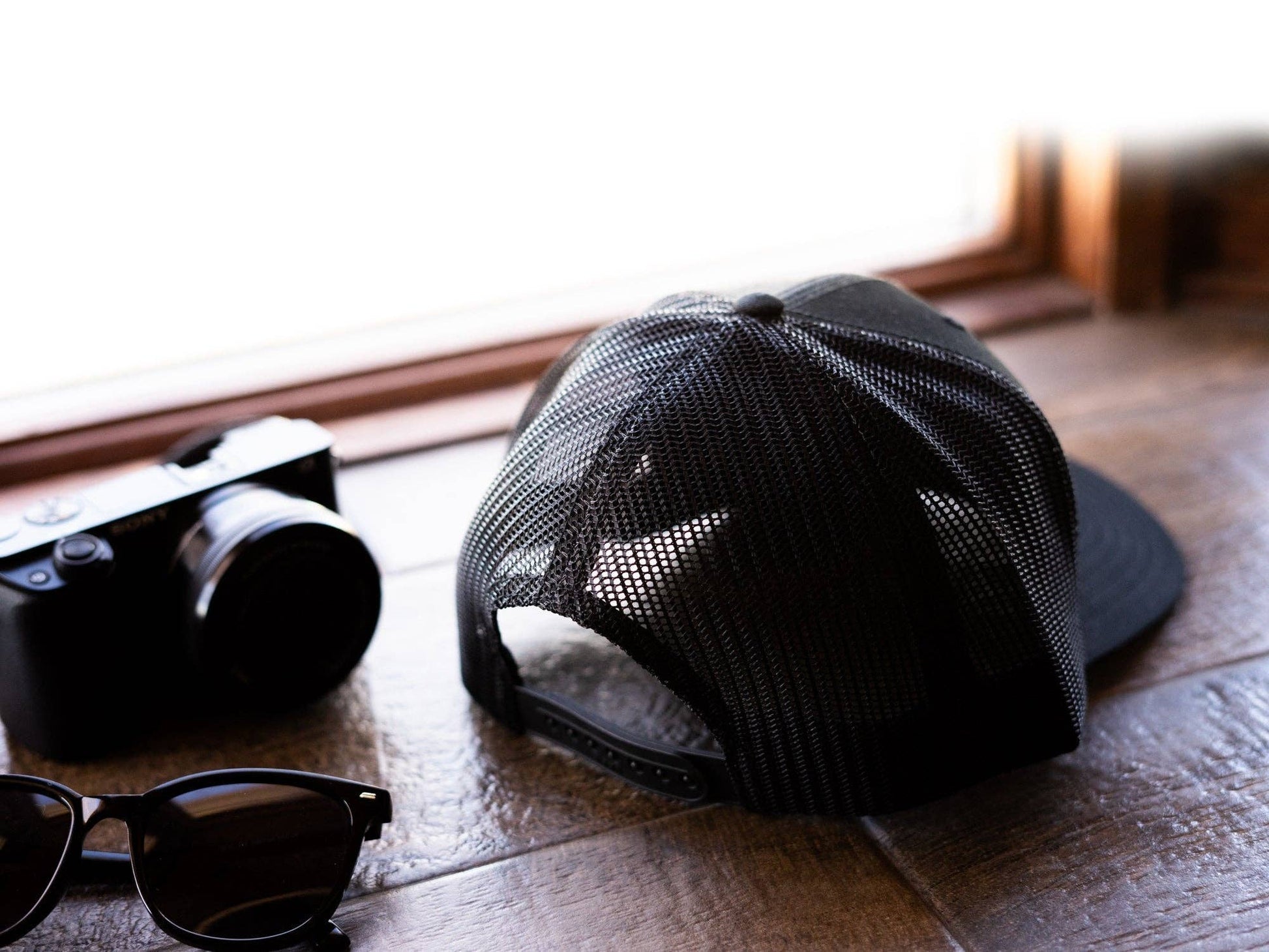Black mesh cap and sunglasses on a wooden surface with a blurred background