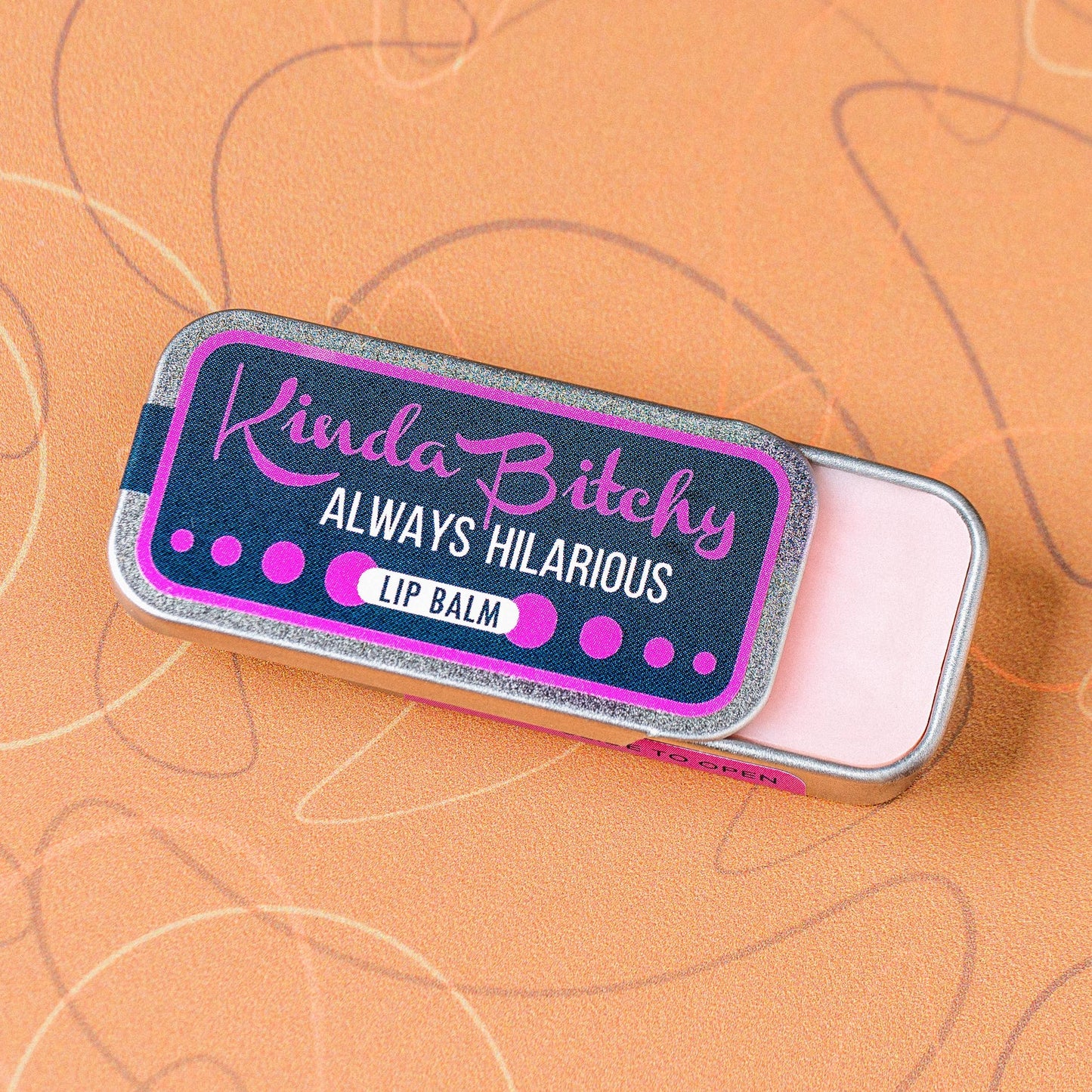 Lip balm tin with humorous label on a peach background