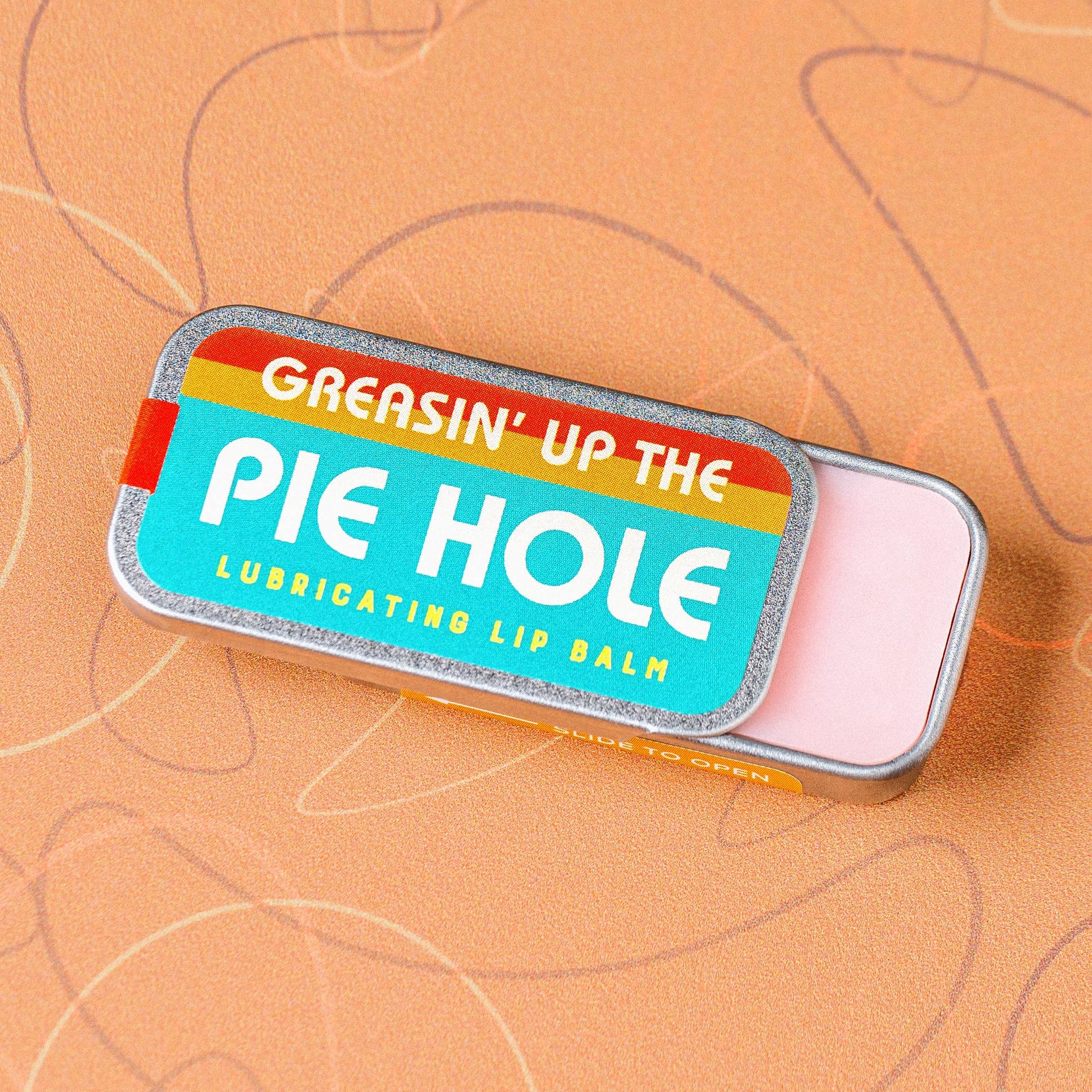 Lip balm tin with colorful label and humorous text on a textured brown background